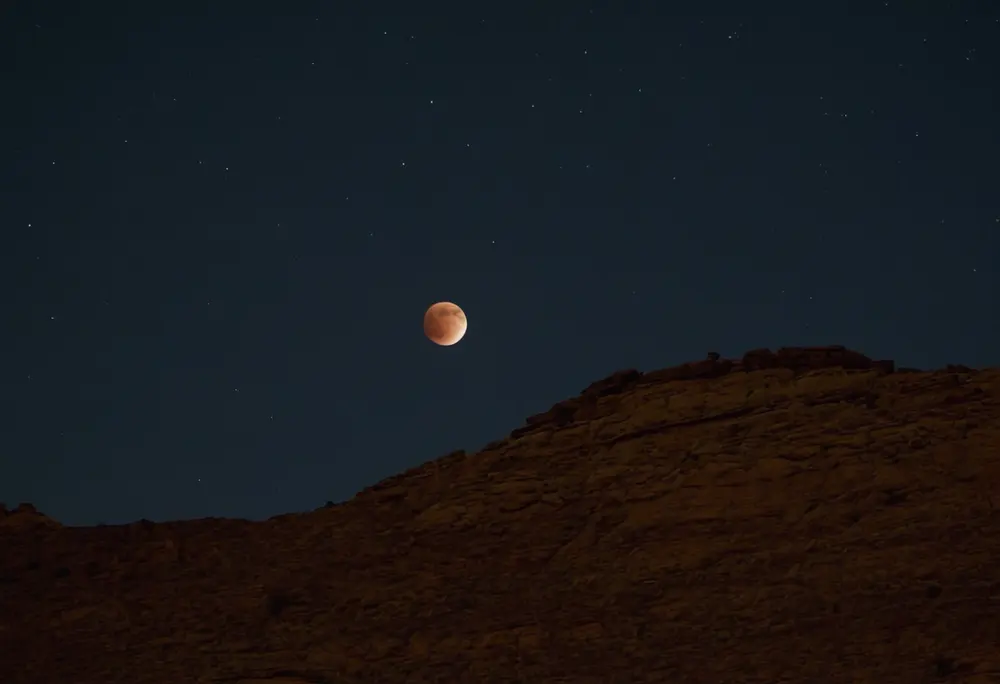 Eclipsed moon above a dark desert ridge