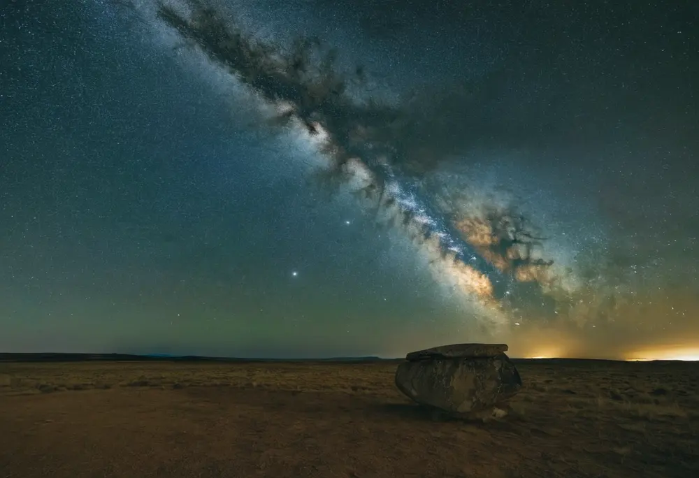 Milky Way arching over a plain with a standing stone
